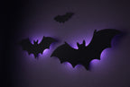 Gros plan de trois chauves-souris noires en plastique avec halo violet, dans le noir