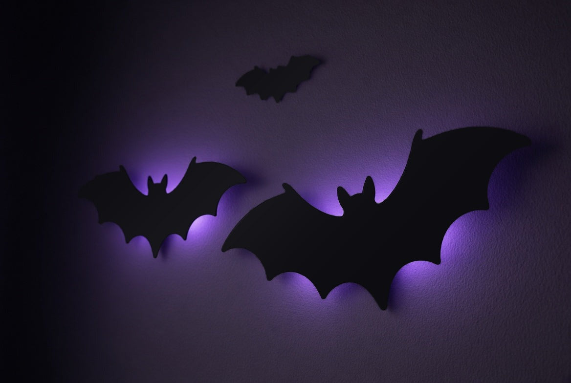 Gros plan de trois chauves-souris noires en plastique avec halo violet, dans le noir